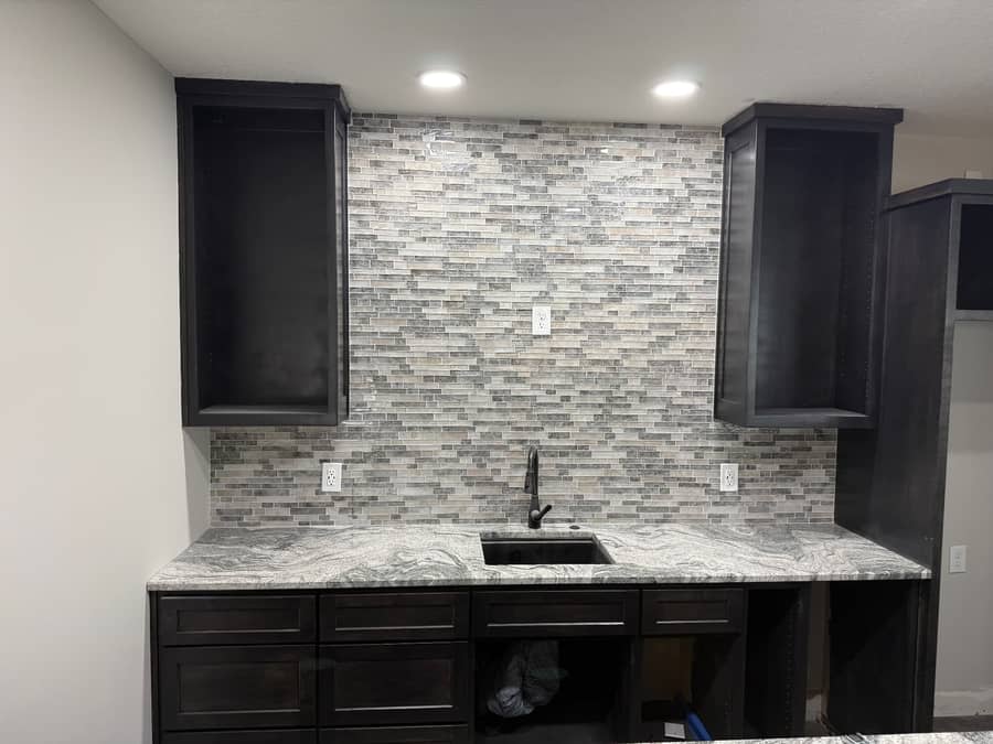 Basement wet bar built by Revived Spaces with dark cabinetry, granite counter, and stacked stone backsplash